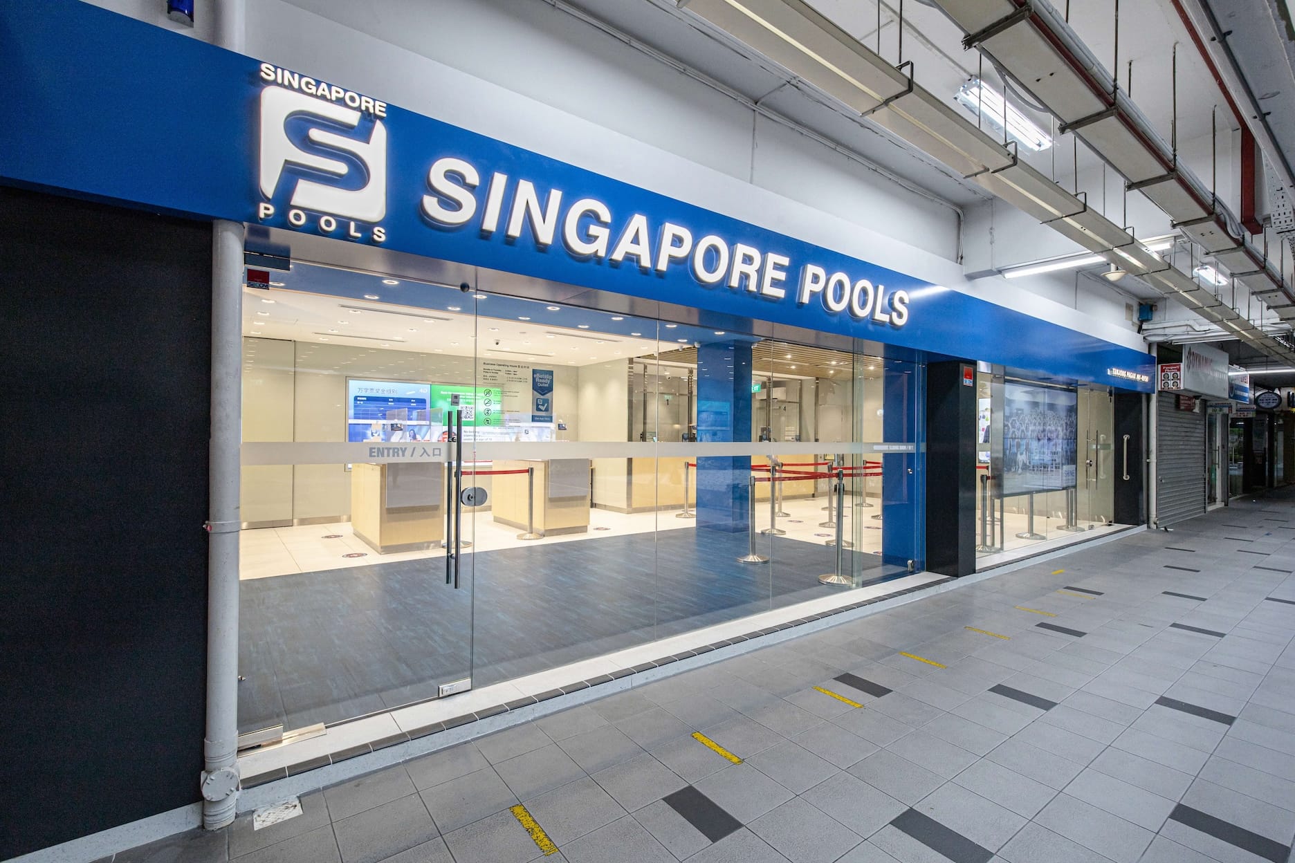 Storefront for Singapore Pools with glass doors and social distancing cues.
